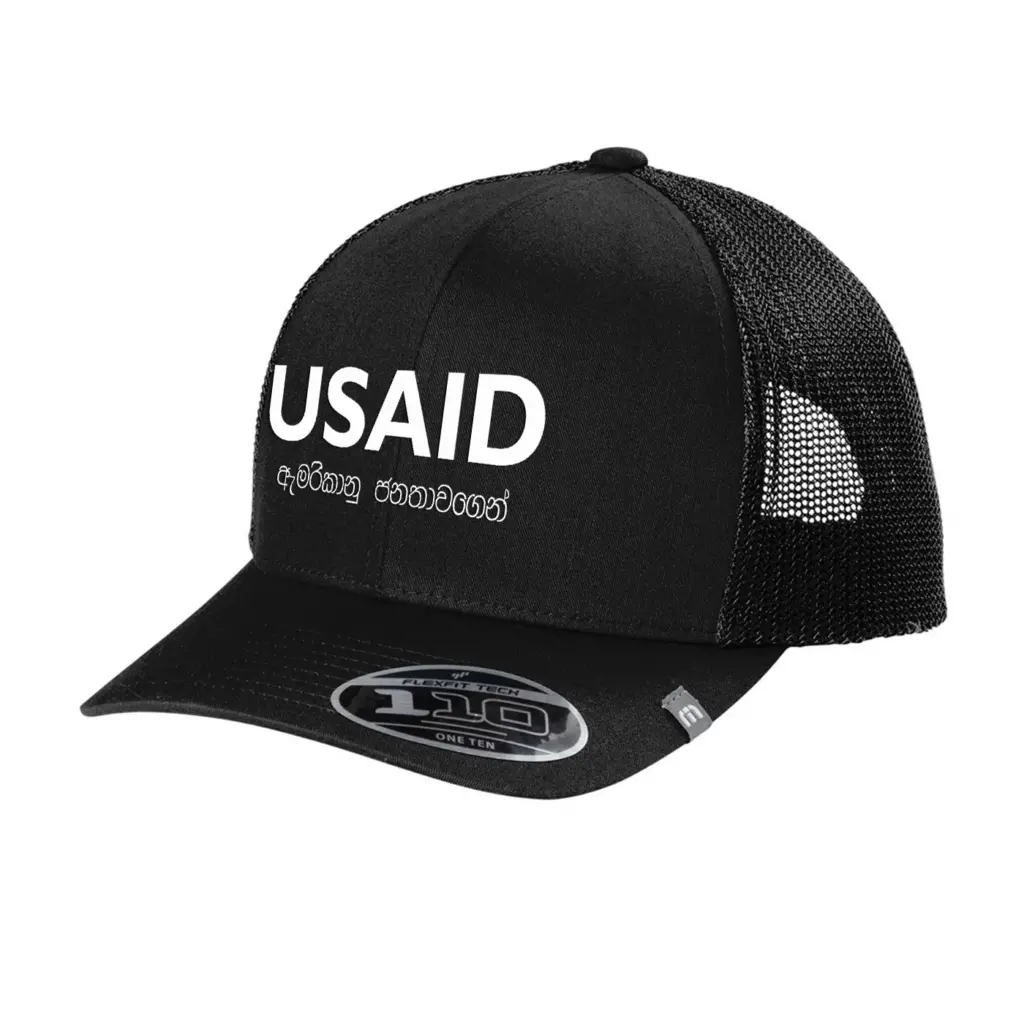 USAID Sinhala - Embroidered New TravisMathew Cruz Trucker Cap (Min 12 pcs)